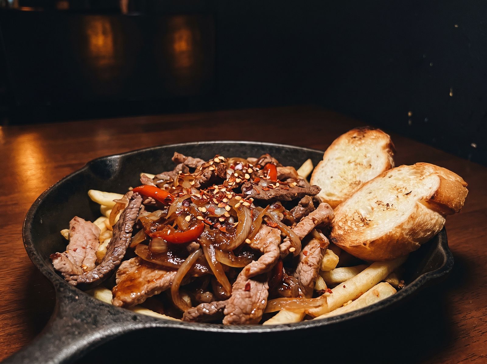Chorrillana en sartén de hierro con cebolla, peppers y pan tostado
